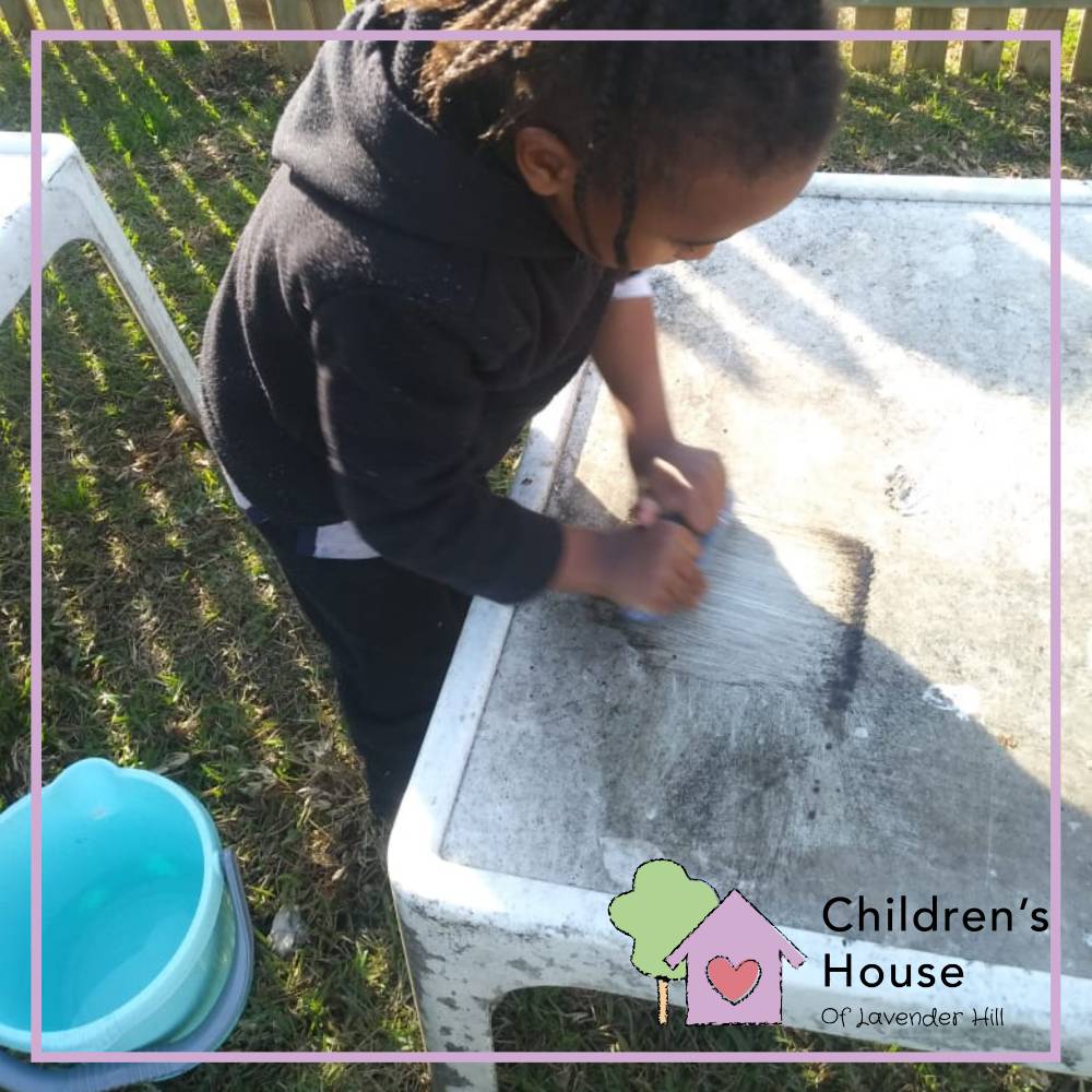 Children learn to take care of their environment. Here a child is scrubbing a donated table for our outside area. This is a great physical activity, and the children love playing with water while they accomplish something valuable to the school community.